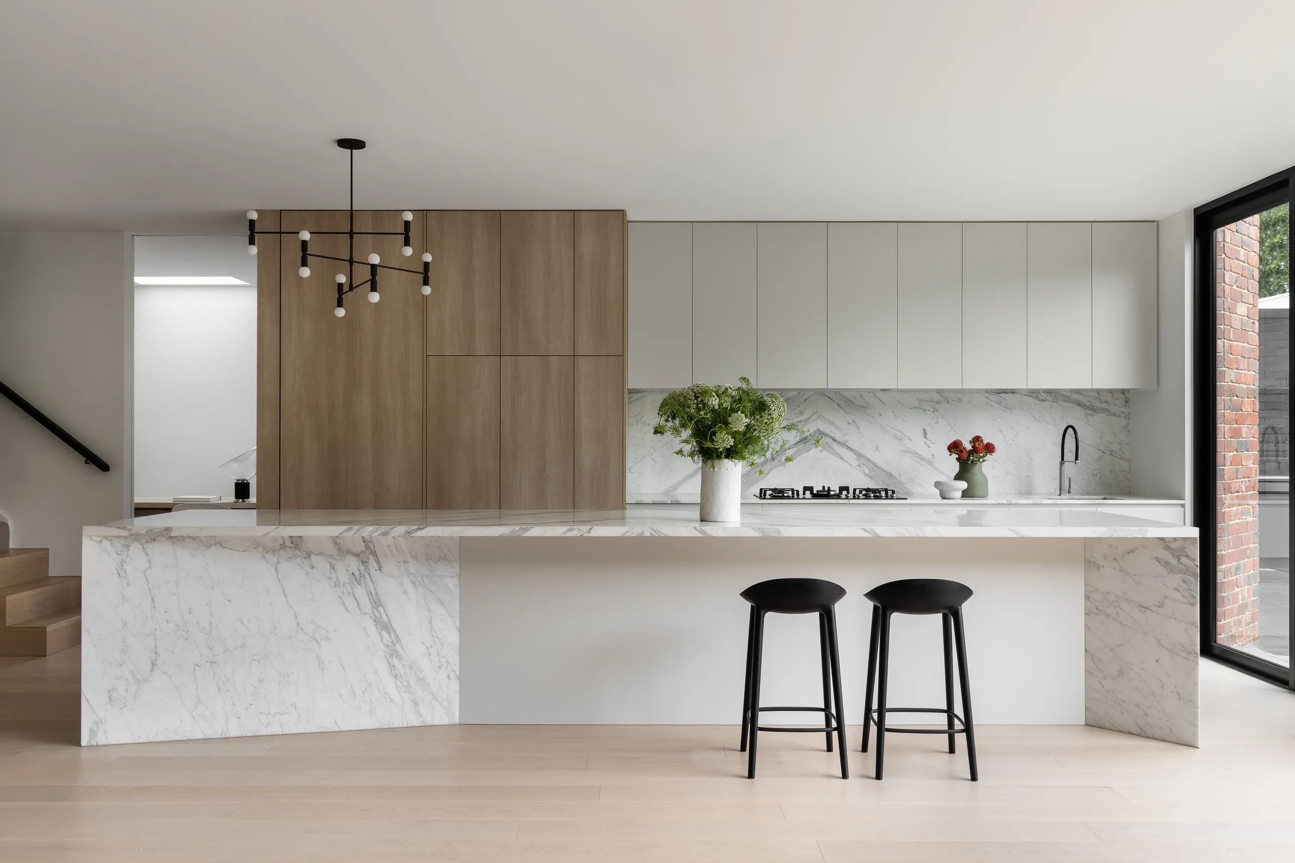 Kitchen with a marble island bench, timber joinery and a black pendant light