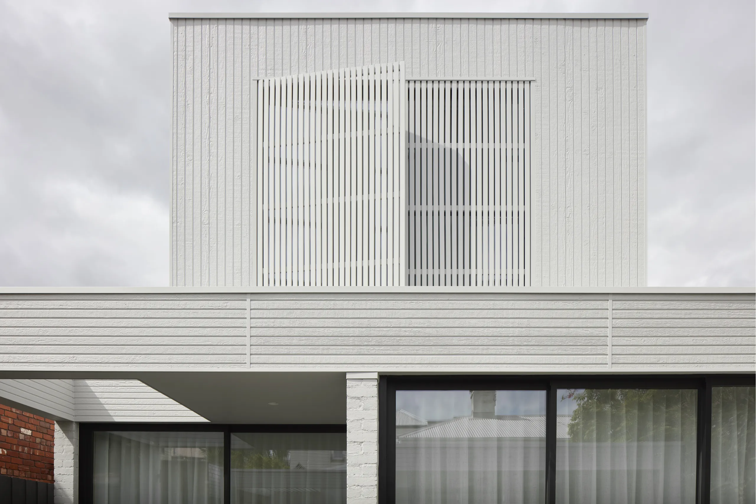 White vertical screen facade above a battened fence and glazed ground floor